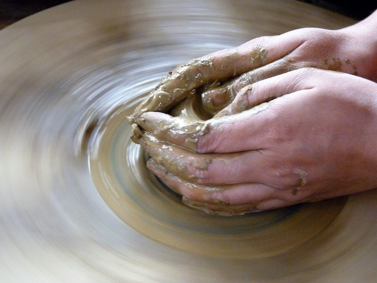 Closeup of hands making small pot on pottery wheel
