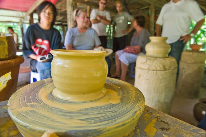Wet clay pot sits on wheel with people in the background