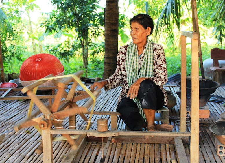 Older Khmer woman sits at large loom