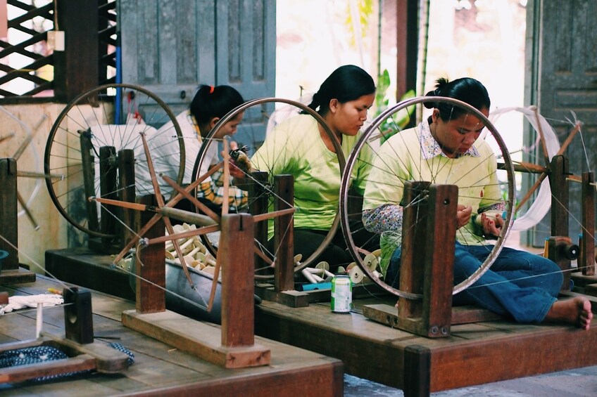 Women sit next to large round looms used to weave silk