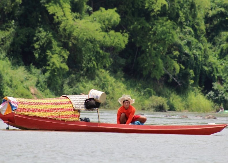 Man kneels in long red boat on the Nam Ou River