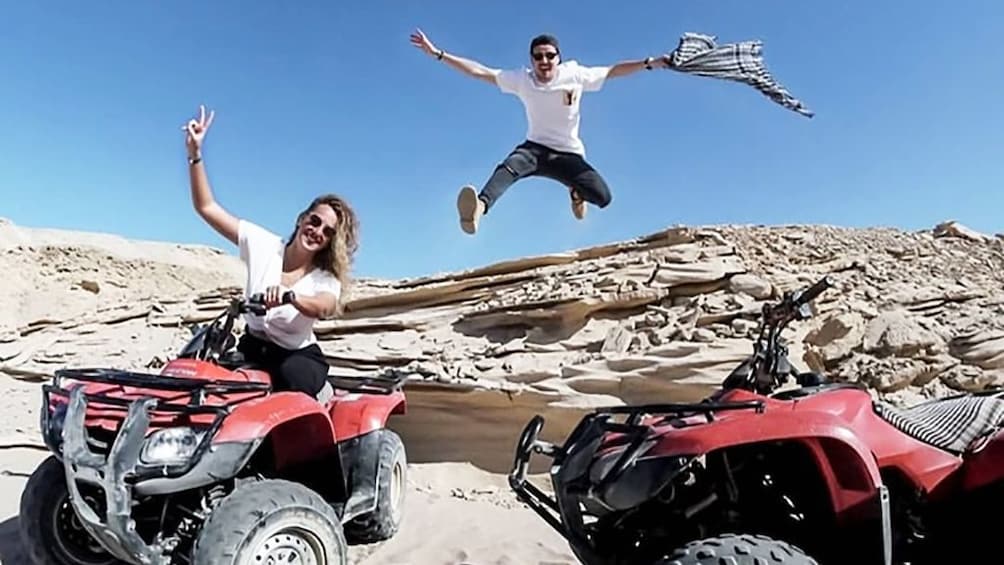 Woman poses on quad while man jumps in the air holding a scarf in Egypt