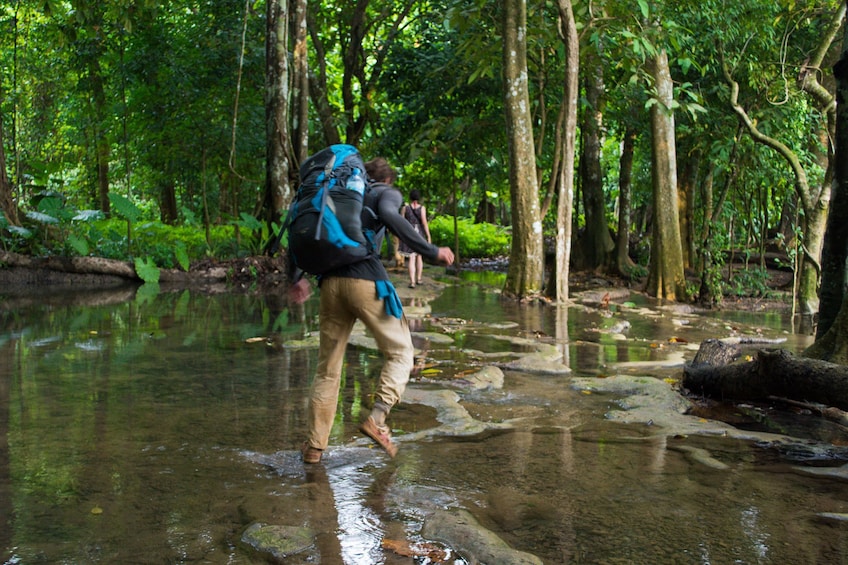 Man with backpack treks through creek in Kuang Si, Laos