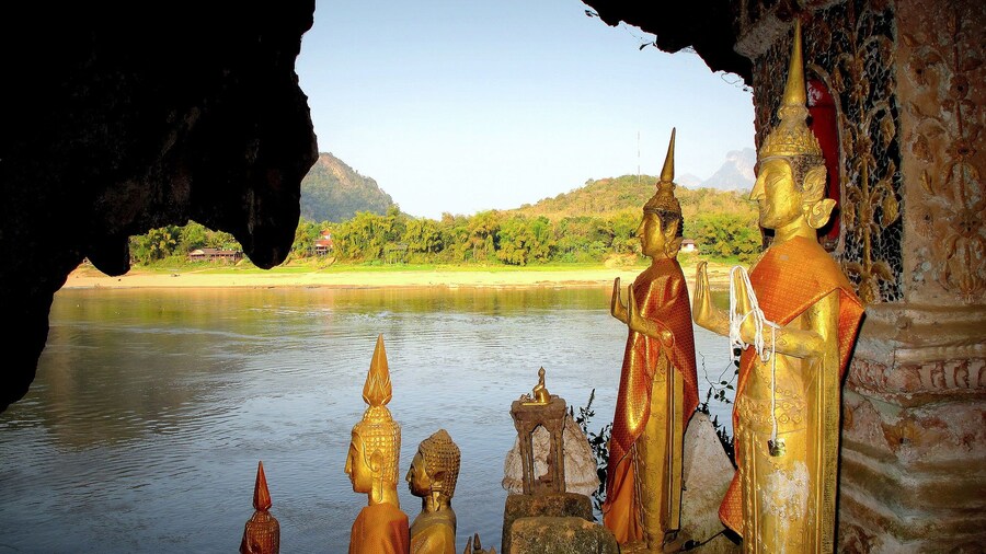 Golden Buddha statues with water in the background at Pak Ou Caves in Laos