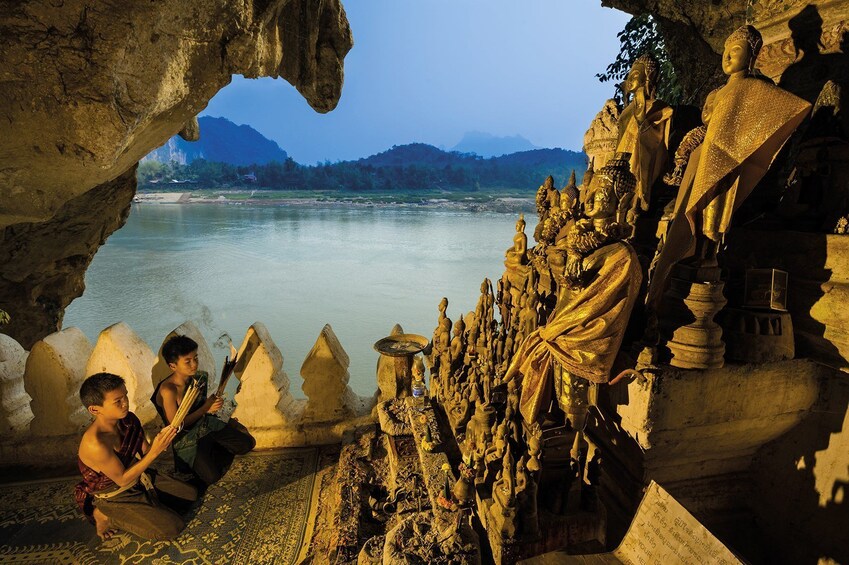 Young boys pray in front of Buddha statues at Pak Ou Caves in the evening