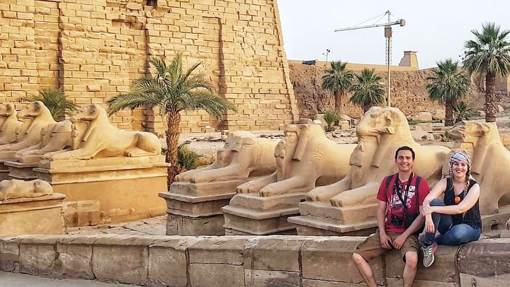 Couple sit on short wall in front of Karnak Temple in Luxor, Egypt