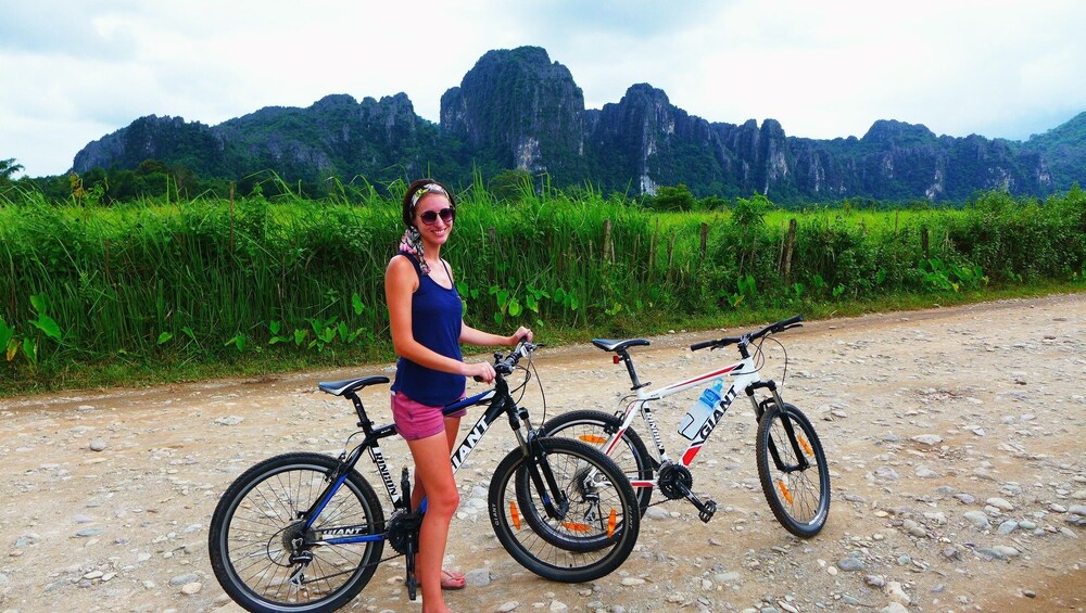 Woman poses on bike on dirt road with mountains in the background