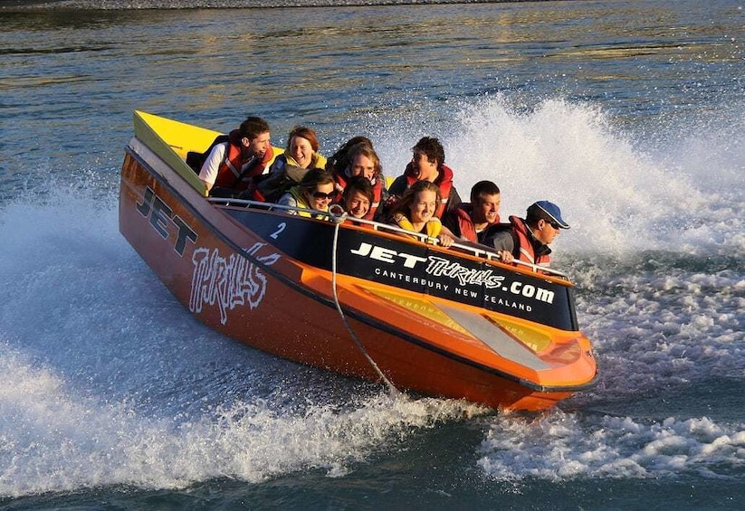 Orange jet boat rides a large wave on Waimakariri River