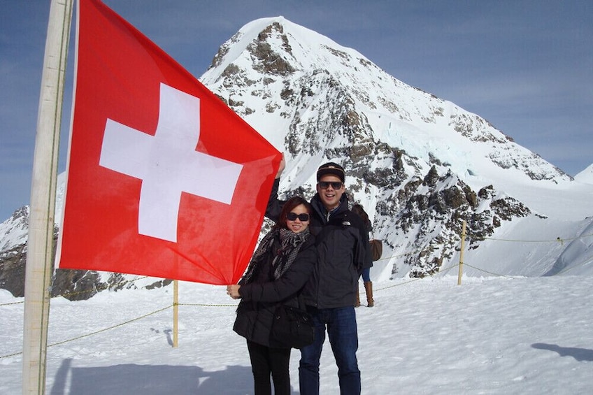 Two people posing next to the Swiss flag at Jungfraujoch Saddle in Switzerland