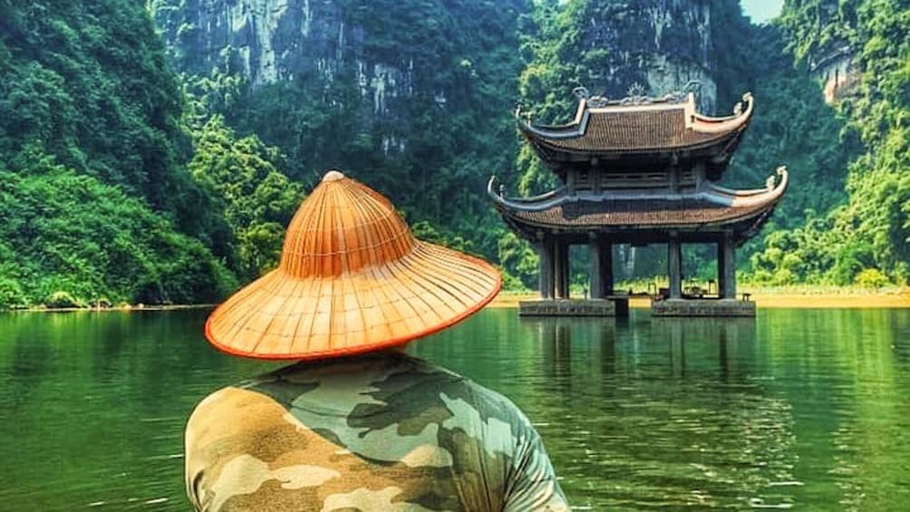 Man in hat looks out at water and pagoda in Ninh Binh, Vietnam