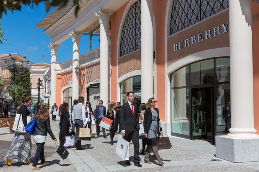 Shoppers walk by Burberry store at Castel Romano shopping mall