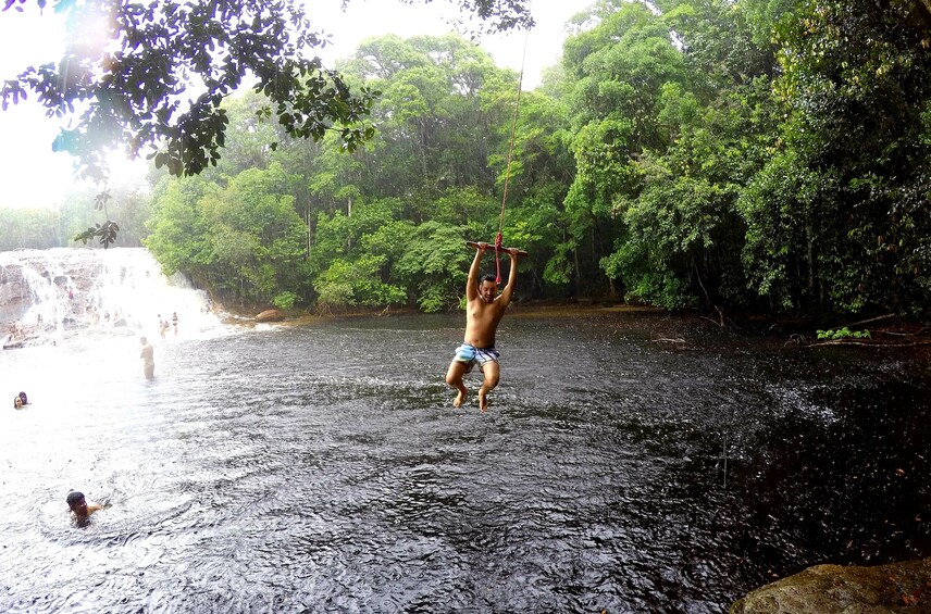 Man in swimsuit swings over lake in Presidente Figueiredo, Brazil