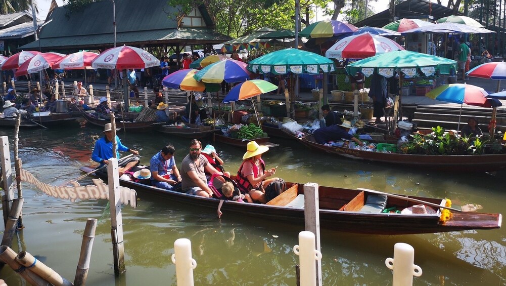 Boat of tourists riding through the Tha Kha Floating Market in Thailand