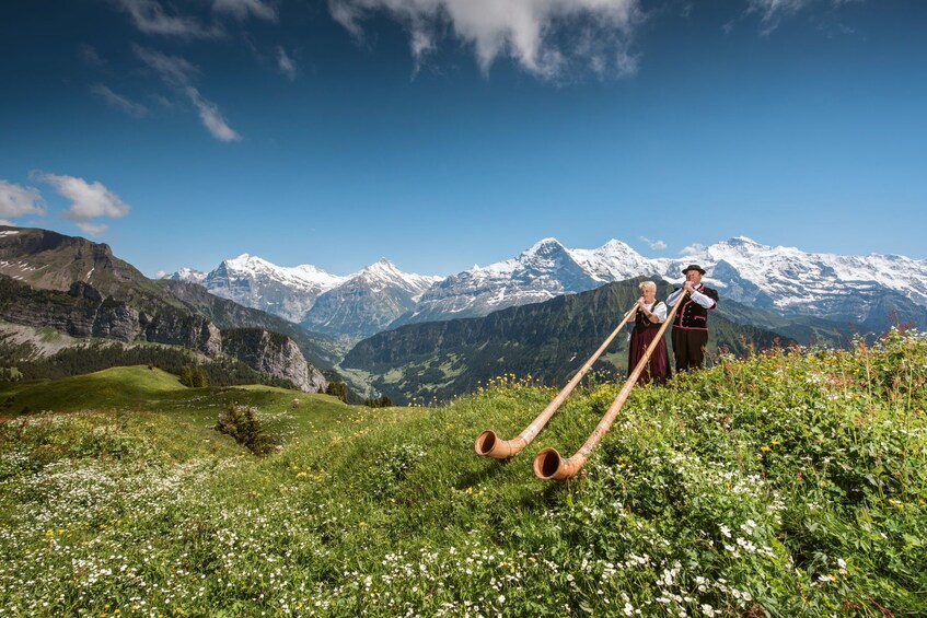 Man and woman play alphorns in the Swiss Alps