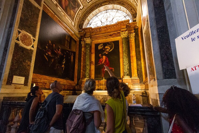 Tourists look at painting at the Church of St. Louis of the French in Rome, Italy