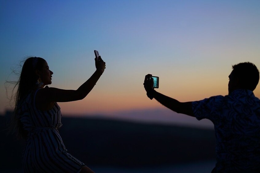 Man and woman take pictures of the Mediterranean coast at dusk