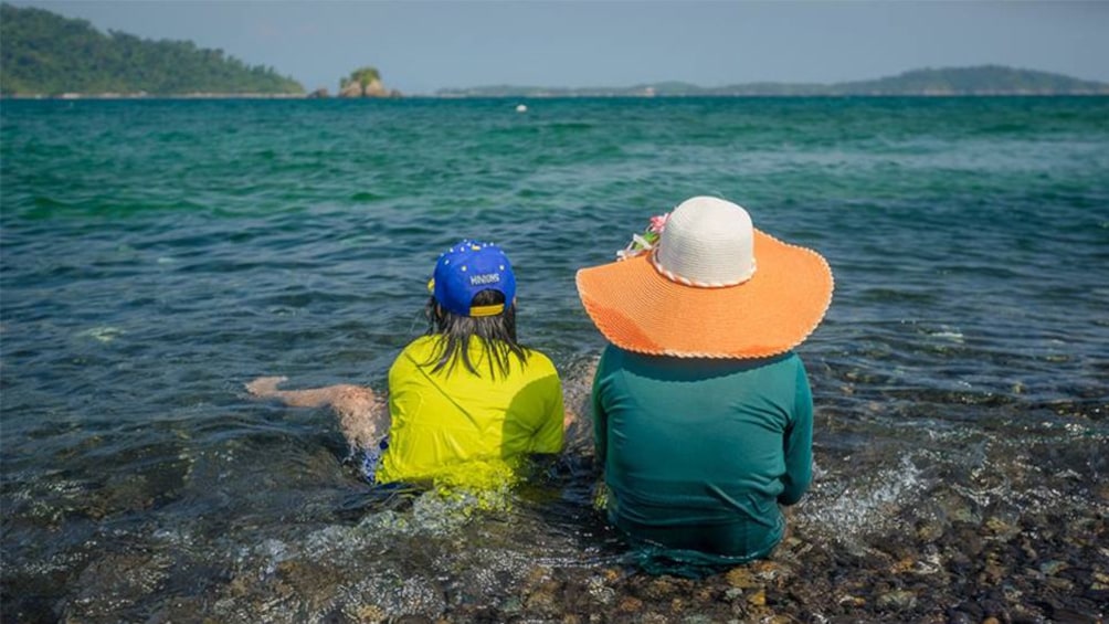 Two people sitting in the water on a beach in Thailand