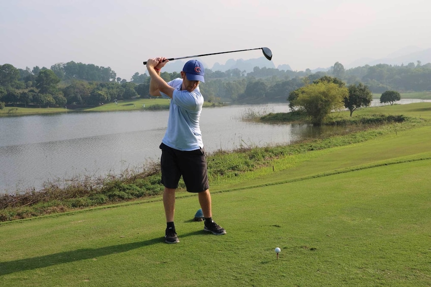 Man swings golf club near lake on golf course