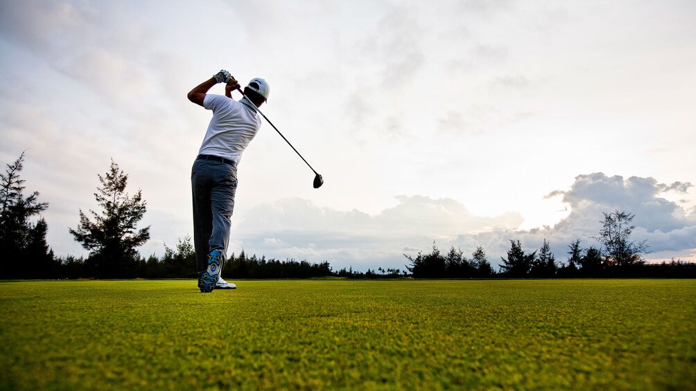 Golfer swings club on course on a cloudy day