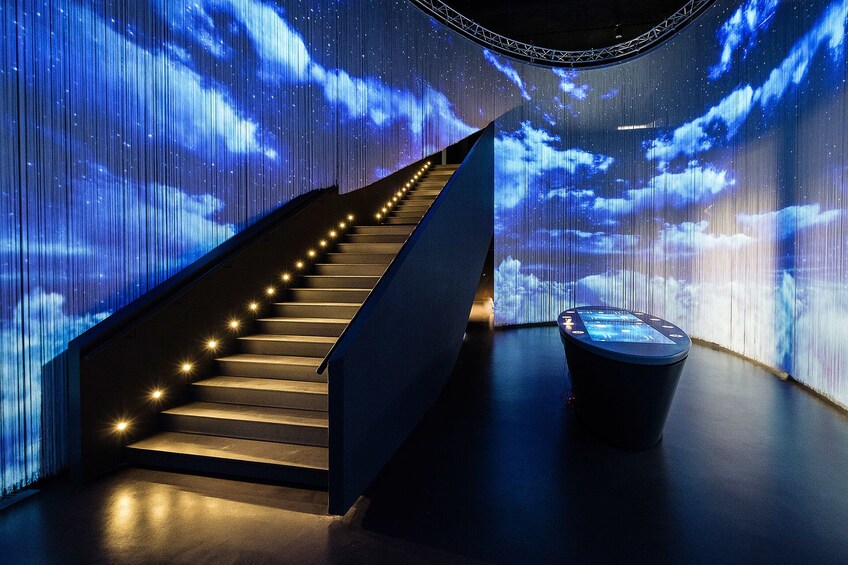 Dark room with lit staircase and projected clouds on walls