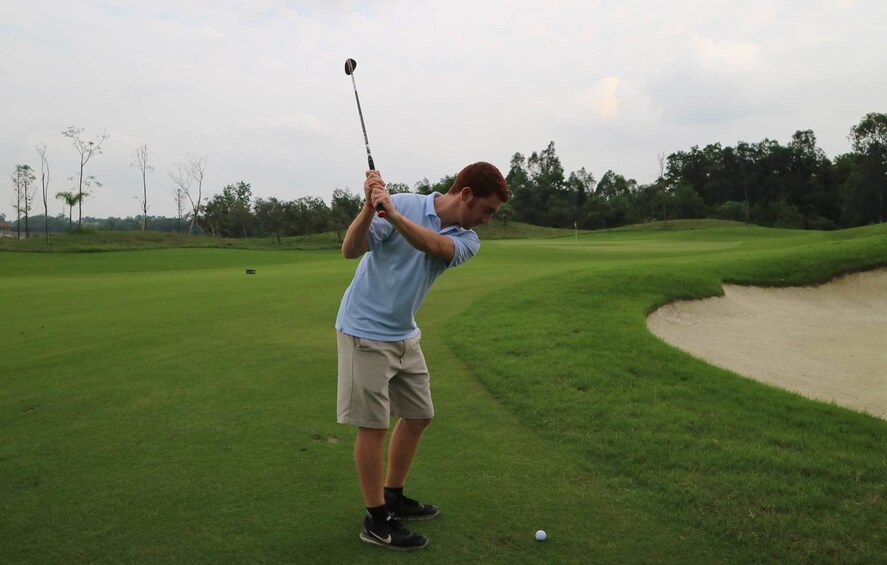 Man swings golf club near sand trap