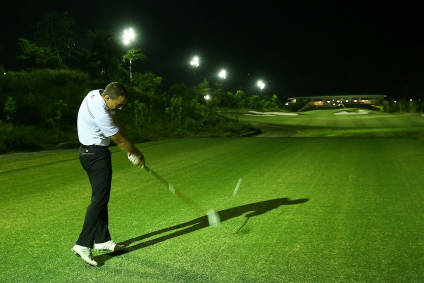 Man hits golf ball on course at night in Vietnam