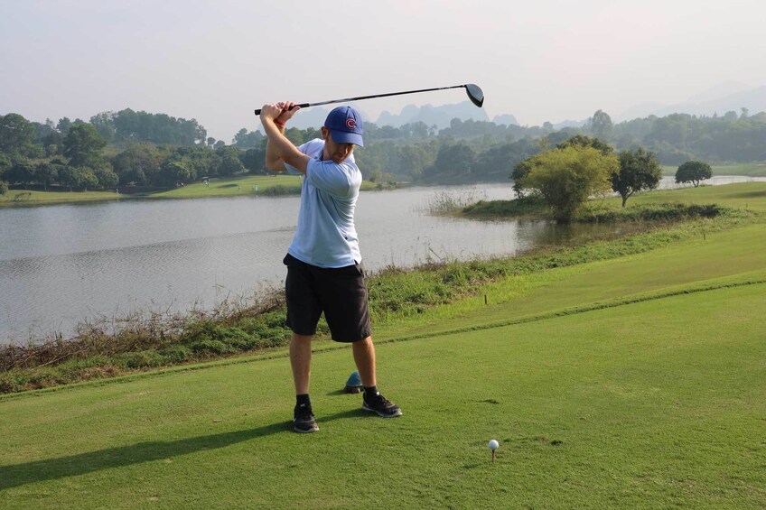 Man swings golf club near lake at Dalat Palace Golf Club
