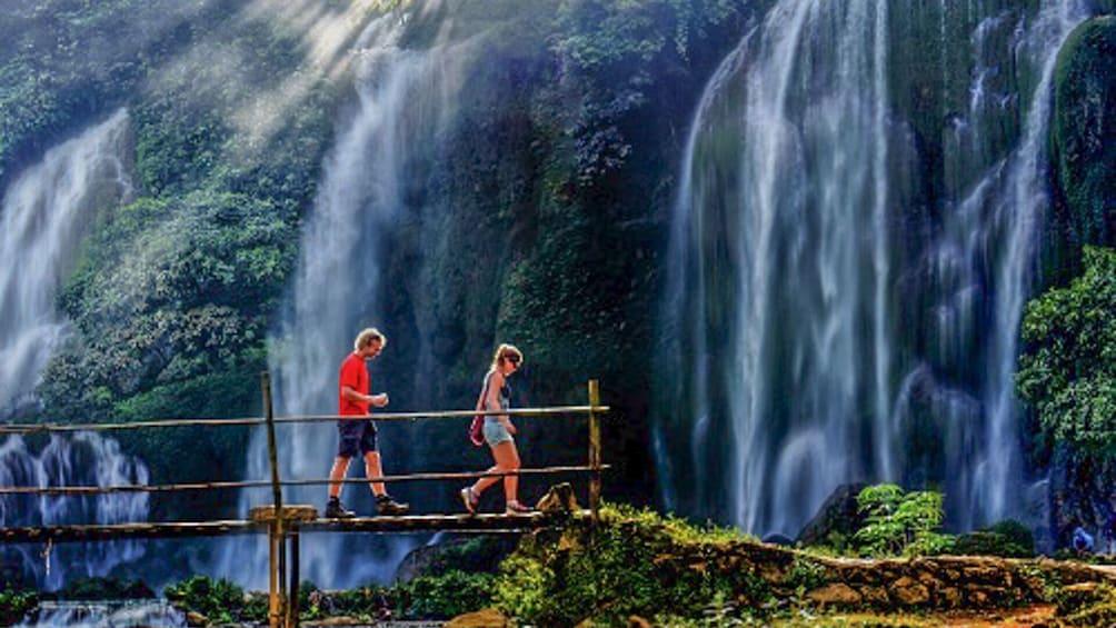Tourists walk along small bridge at Ban Gioc Waterfall