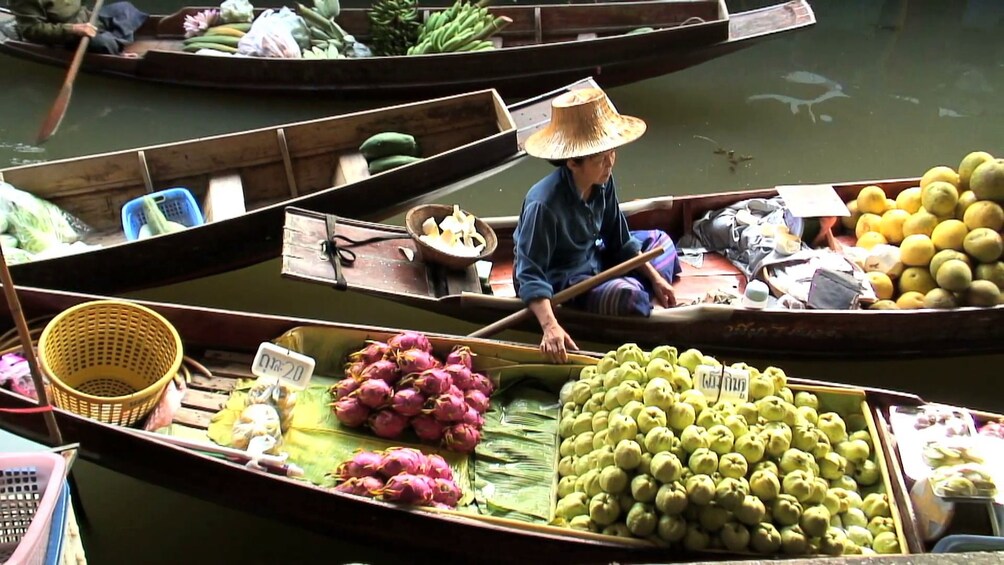 Woman sits in a boat and hold another filled with fruit