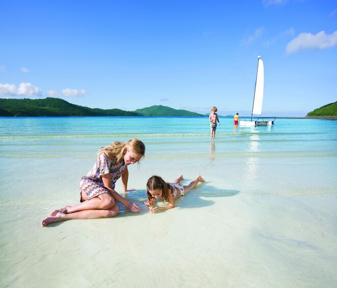 Woman and girl sit on the beach of Hamilton Island