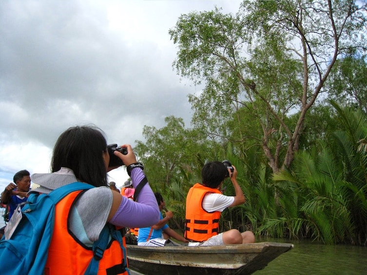 Tourists take pictures from boats of bird in tree in Thailand