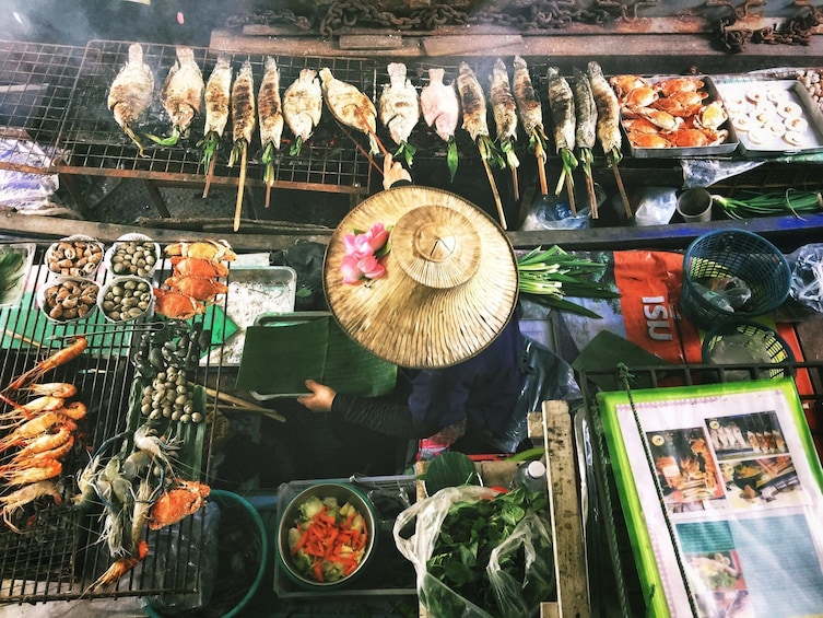 Woman grabs fish off of grill in Bangkok market