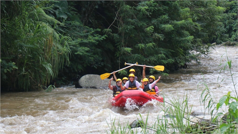 Show item 1 of 9. River rafters hold their paddles up on river in Bali