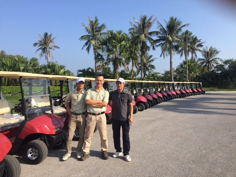 Three golfers pose with long line of golf carts at Vietnam golf club