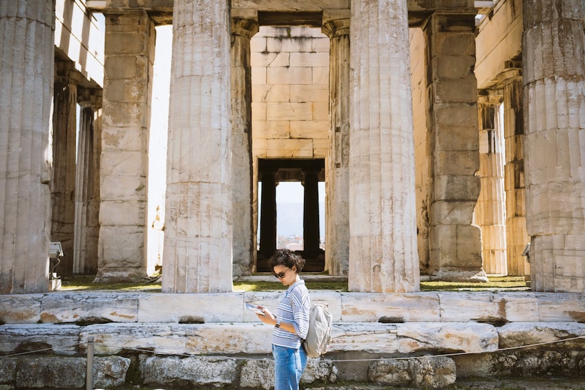 Woman looks at a travel book while standing next to the Acropolis