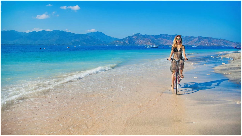 Show item 2 of 7. Woman bikes along the beach on the Gili Islands