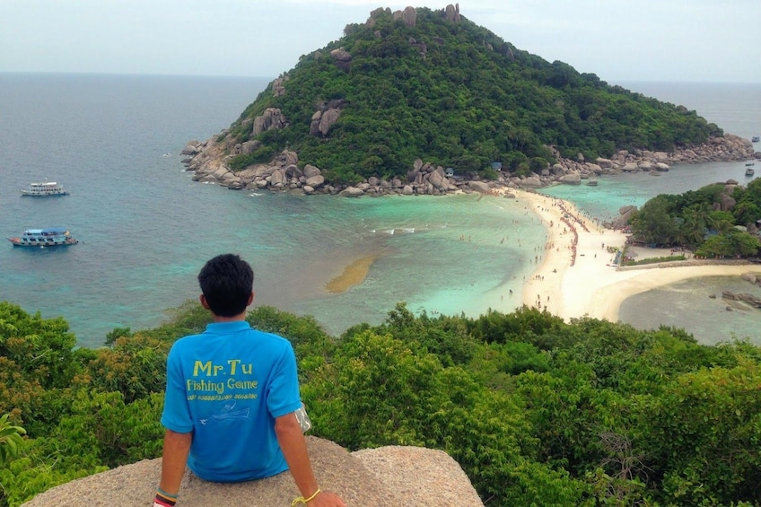Tour guide sits on rocks looking out towards Nang Yuan Island