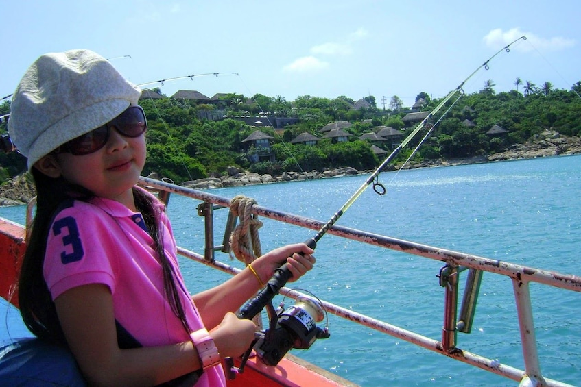 Little girl holds fishing pole on boat in the Gulf of Thailand
