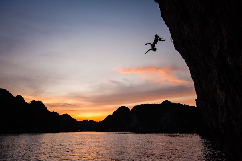 Person jumps off cliff into water on Cat Ba Island at sunset