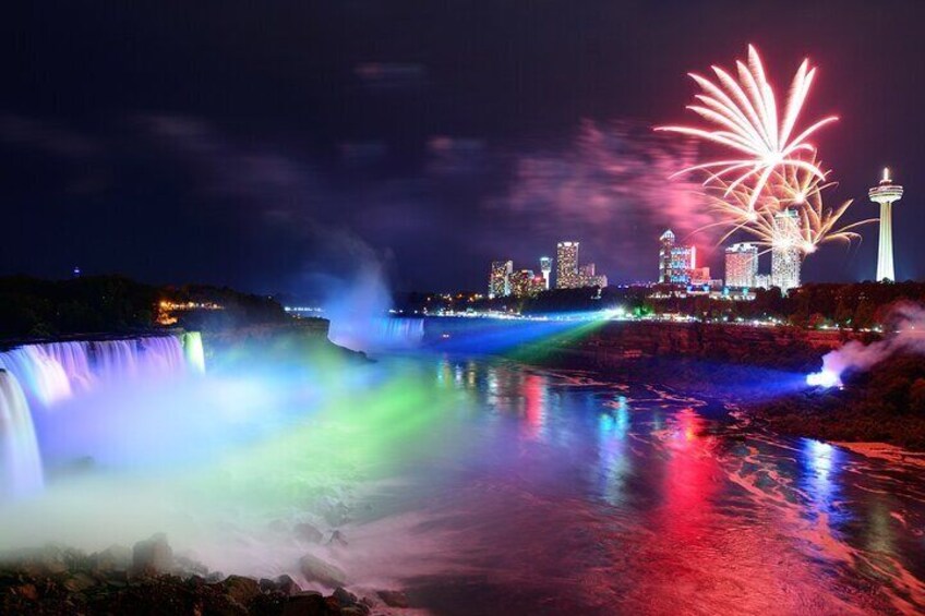 Niagara Falls lit at night by colorful lights with fireworks.