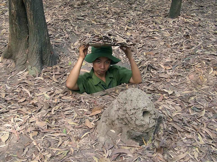 Man stands in camouflaged entrance to Cu Chi Tunnels 