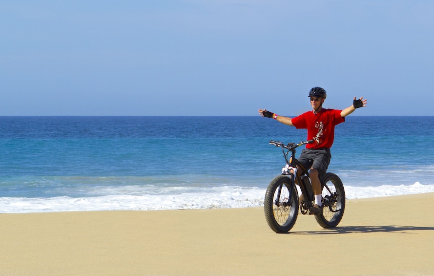 Man rides electric bike with no hands on beach in Los Cabos