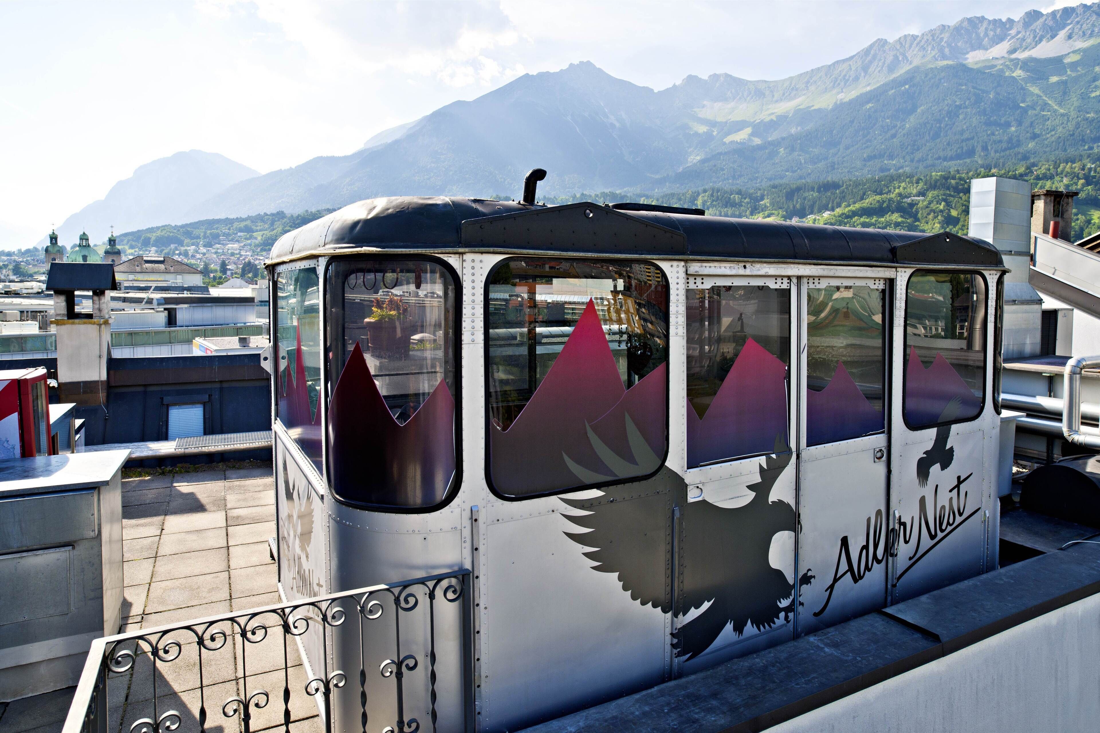 A terrace with wicker chairs and tables, overlooking a mountainous landscape with snow-capped peaks.