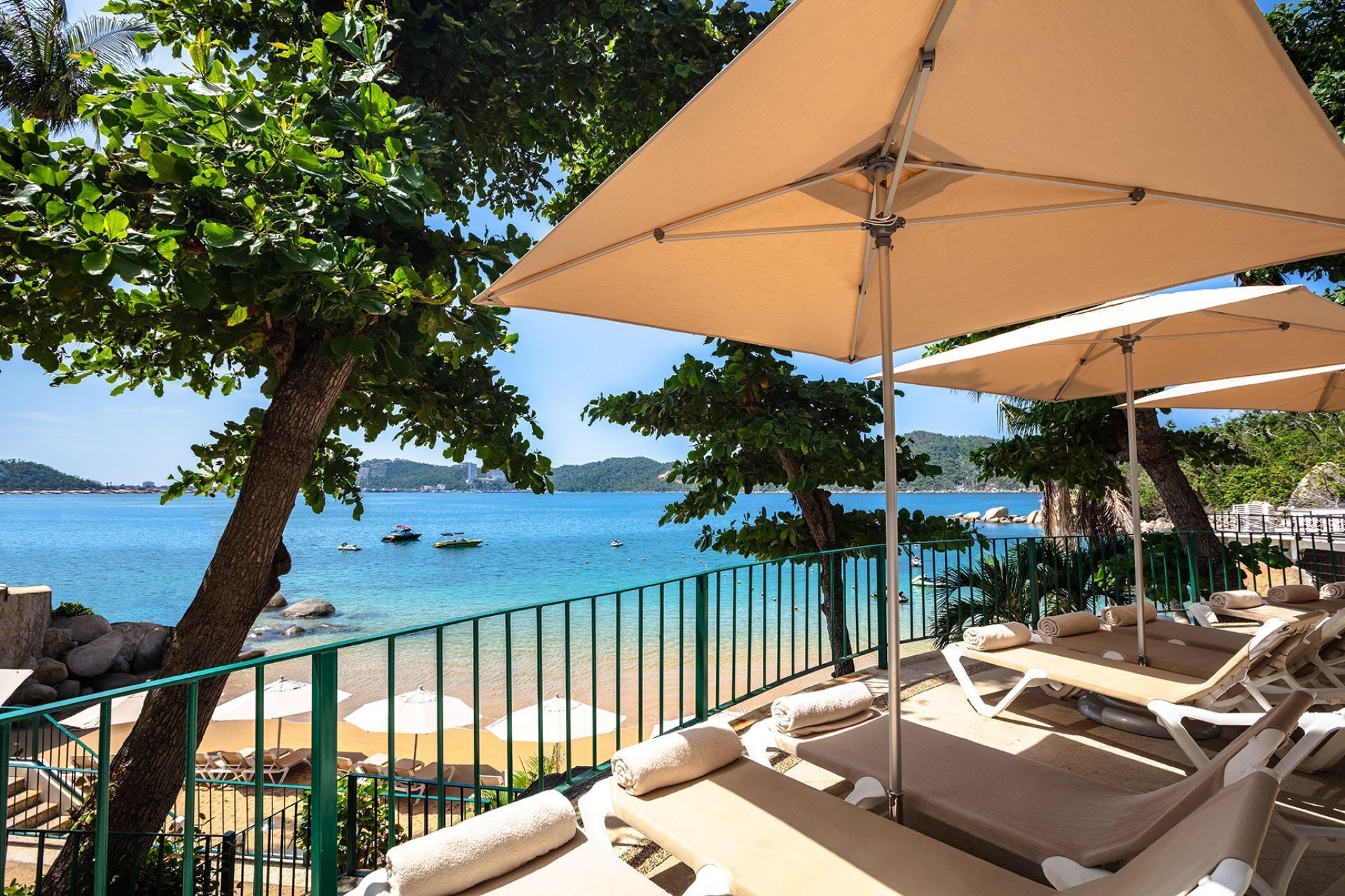 A seaside restaurant with tables and chairs arranged for dining, overlooking a clear blue sea with boats.