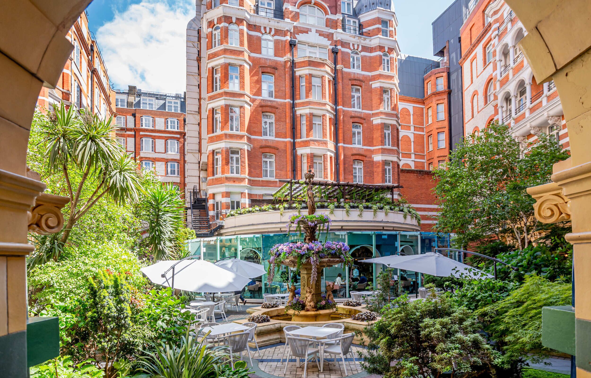 A courtyard with a central fountain, surrounded by lush greenery and a glass balustrade.
