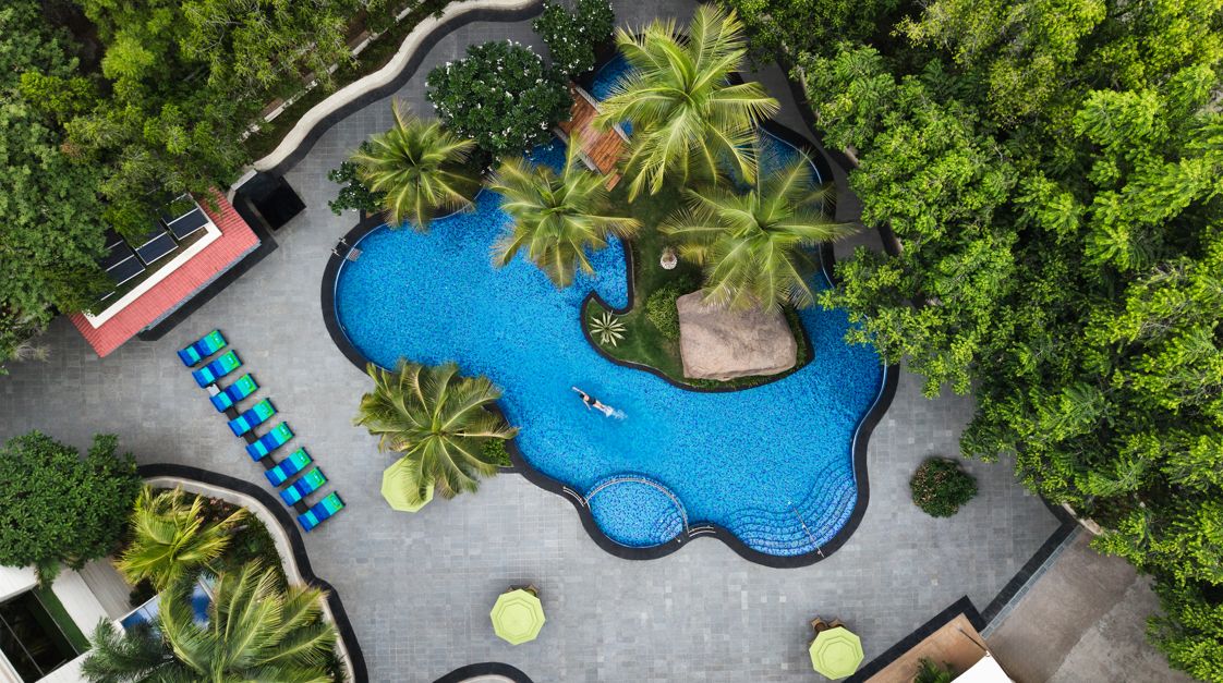 Ein mehrstöckiges Hotel mit Pool, Palmen und Außenbereich.
