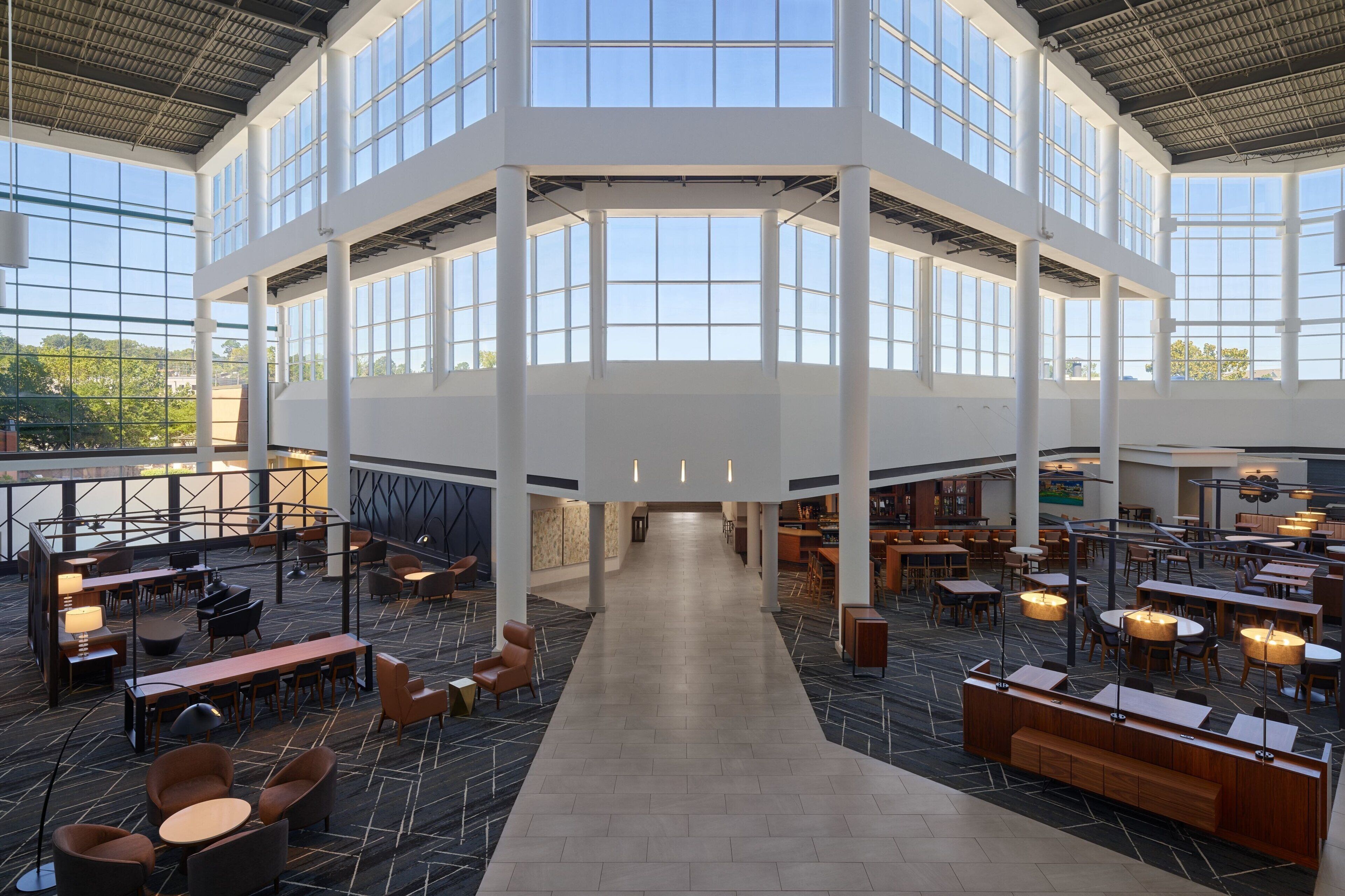 A spacious indoor area with multiple seating arrangements, large windows, and a high ceiling.