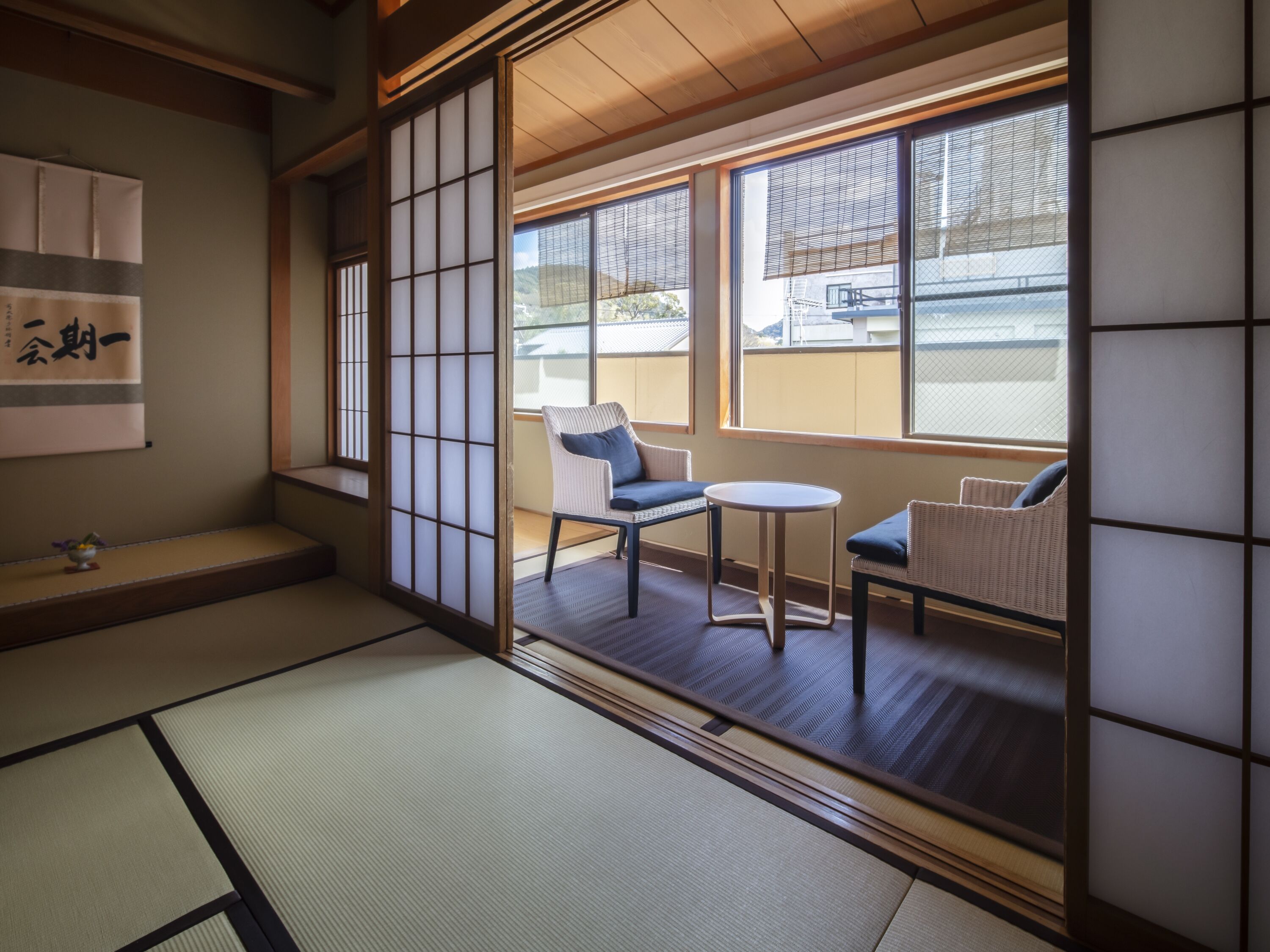 A traditional Japanese room with tatami flooring, shoji screens, and a view of a residential area.
