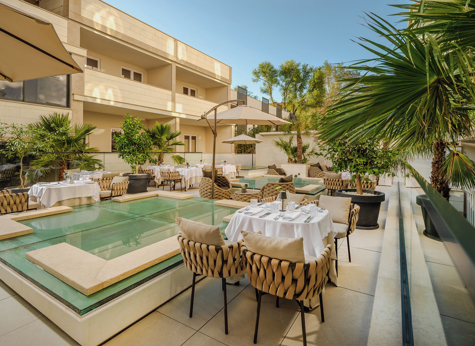 A spacious indoor dining area with multiple tables and chairs, surrounded by lush greenery and potted plants.