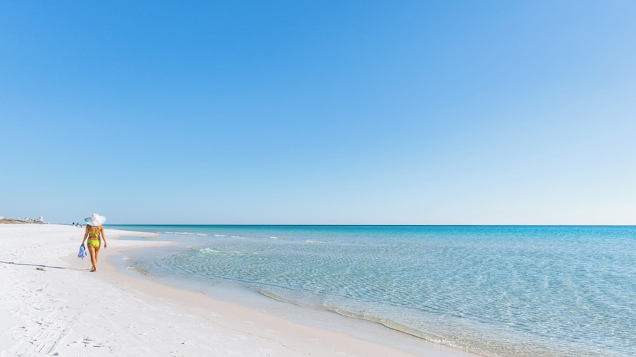 Woman walking on soft white sand at Norriego Point with calm Gulf waters in Destin, Florida.